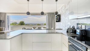 A modern kitchen with a large island, pendant lights, and a view of the sea.