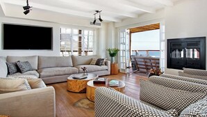 Un vaste salon comprenant un grand canapé, une table basse et un téléviseur à écran plat fixé au mur. Un balcon offre une vue sur la mer.