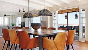 Un vaste espace dédié à la salle à manger, avec une grande table en bois, des chaises en cuir et des lampes suspendues.