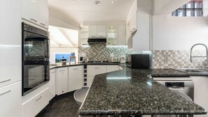 Une cuisine moderne avec des meubles blancs, un plan de travail en granit et un four encastré.