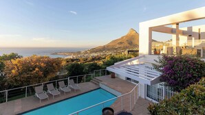 Un espace piscine moderne avec des chaises longues, une vue sur l’océan et une montagne en arrière-plan.