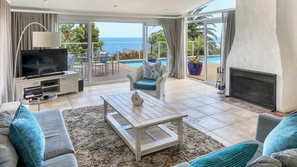 A spacious living room with a television, sofa, and coffee table. It features a large glass door leading to a pool and a view of the ocean. - Ocean Views, Pool, Sleeps 6, Camps Bay - Rontree (Cape Town)