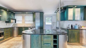 A modern kitchen with green cabinets, a central island, stainless steel appliances, and a window with blinds. - Ocean Views, Pool, Sleeps 6, Camps Bay - Rontree (Cape Town)