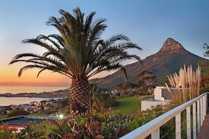 A coastal landscape with a prominent palm tree, a mountain in the background, and a view of a town across the water. - Ocean Views, Pool, Sleeps 6, Camps Bay - Rontree (Cape Town)