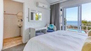 A bedroom with a large bed, a desk, a chair, a window with a view of the sea, and an air conditioning unit. - Ocean Views, Pool, Sleeps 6, Camps Bay - Rontree (Cape Town)