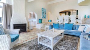 A spacious living room with a fireplace, a blue sofa, a white coffee table, and a modern kitchen in the background. - Ocean Views, Pool, Sleeps 6, Camps Bay - Rontree (Cape Town)