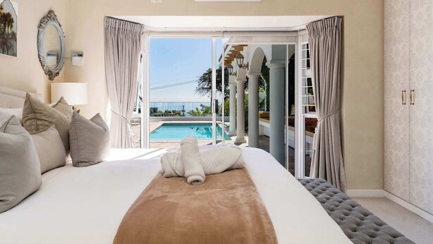 A hotel room with a large bed, a view of a swimming pool, and a balcony with columns.