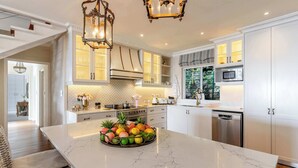 A modern kitchen with white cabinets, a marble island, and a fruit bowl.