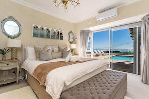 Un dormitorio con una cama grande, una mesita de noche, una lámpara y vista a una piscina a través de un ventanal corredero.