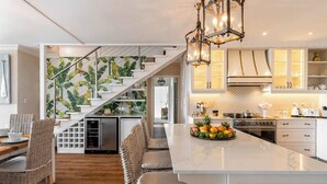A modern kitchen with a central island, stainless steel appliances, and a staircase with a tropical wallpaper design.