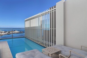 A poolside area with a view of the sea, a white fence, and a lounge chair.