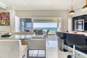 A modern kitchen with a large island, a dining area with a glass table, and a view of the ocean.