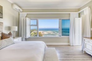 A bedroom with a large window, a bed, a nightstand, and a dresser.