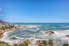 Vista sulla costa con scogliera rocciosa, cielo azzurro e palazzi residenziali.