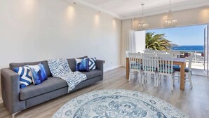 Una sala de estar moderna con un sofá gris, alfombra estampada y una zona de comedor con sillas blancas y una mesa.