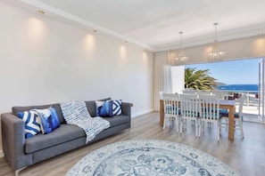 Una sala de estar moderna con un sofá gris, alfombra estampada y una zona de comedor con sillas blancas y una mesa.