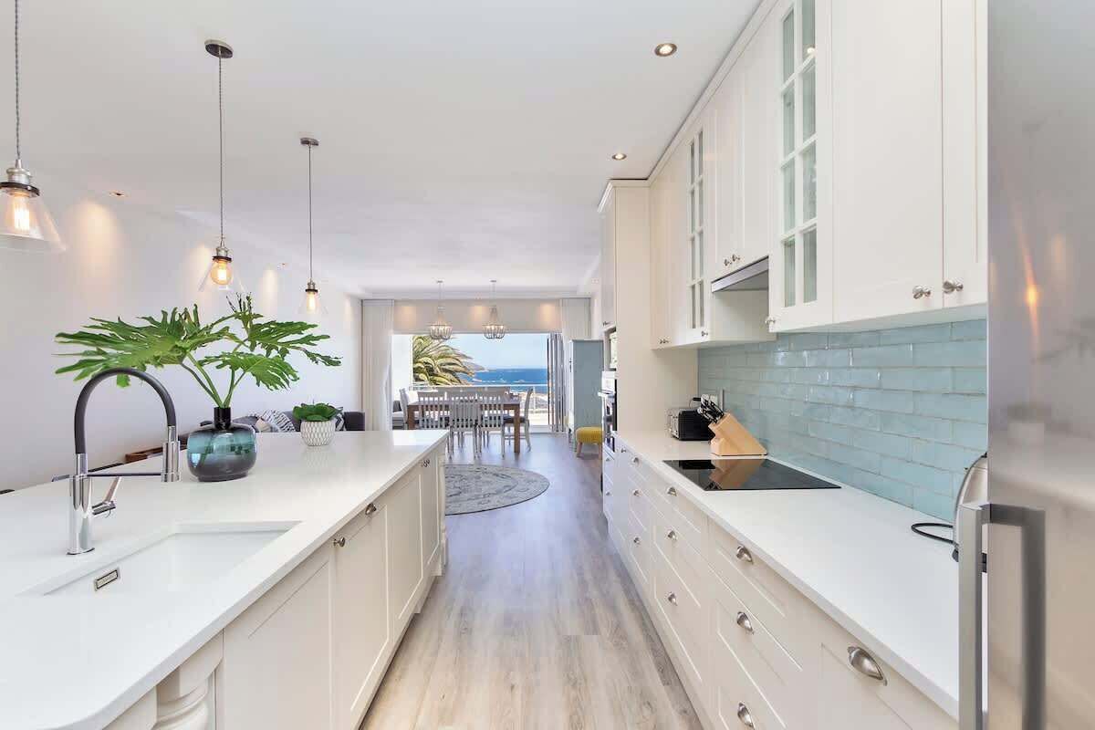 A modern kitchen with white cabinetry, a central island, pendant lighting, and a view to the outdoors.