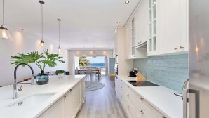 Una cocina moderna con armarios blancos, una isla central, iluminación colgante y vistas al exterior.