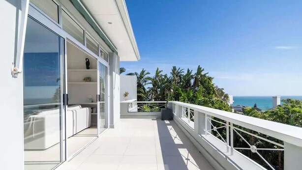 Un balcon moderne avec une porte vitrée, des rampes blanches et une vue sur l’océan.