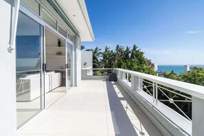 A modern balcony with a glass door, white railings, and a view of the ocean.