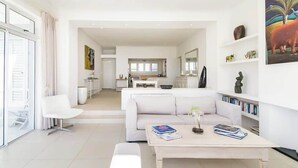 Un salon moderne avec un canapé blanc, une table basse sur laquelle sont posés des livres, et une cuisine en arrière-plan.