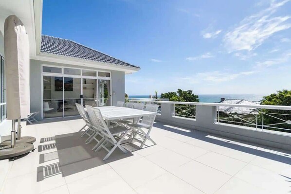 A terrace with a table and chairs, a glass door entrance, and a view of the sea.