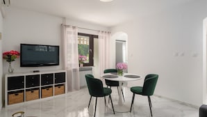 A modern living room with a TV, a dining table with chairs, a sofa, and a view of the outdoors. - Quiet location, 3 persons, air-conditioned, garden with barbecue (Porec)