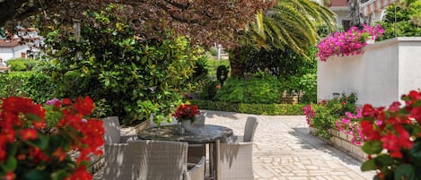 An outdoor patio with wicker furniture, a stone floor, and lush greenery.