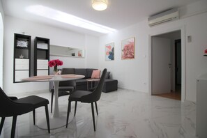 Ein modernes Wohnzimmer mit Essbereich, einem grauen Sofa, einem Couchtisch und einer Vase mit Blumen.