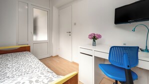 A bedroom with a bed, a desk, a chair, a television, and a vase with flowers. - Quiet location, 3 persons, air-conditioned, garden with barbecue (Porec)