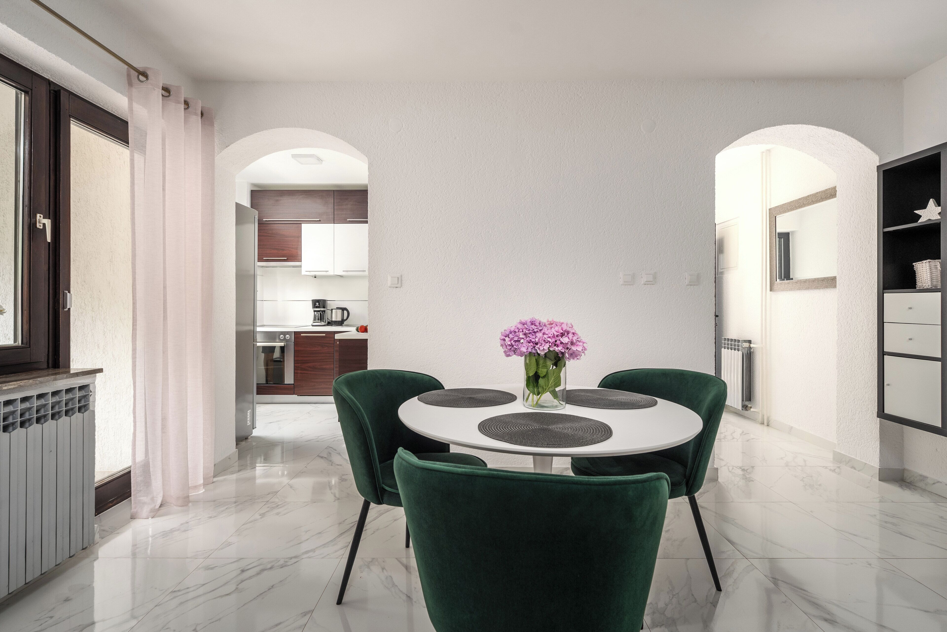 Un espace repas moderne avec une table ronde, des chaises vertes et un vase de fleurs.