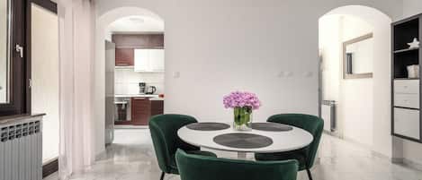 Un comedor moderno con una mesa redonda, sillas verdes y un jarrón de flores.