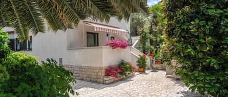 A courtyard with a white building, stone paving, and lush greenery.