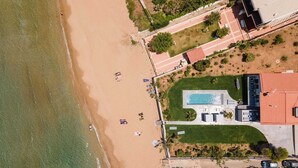 An aerial view of a beachside property with a swimming pool, beach umbrellas, and a parking area.
