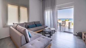A modern living room with a grey sofa, a small round table, and a view of the sea through a glass door.