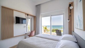 A hotel room with two beds, a TV, and a balcony with a view of the sea.
