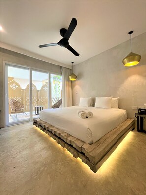 A modern bedroom with a large bed, a ceiling fan, and a view of the outside through a sliding glass door.