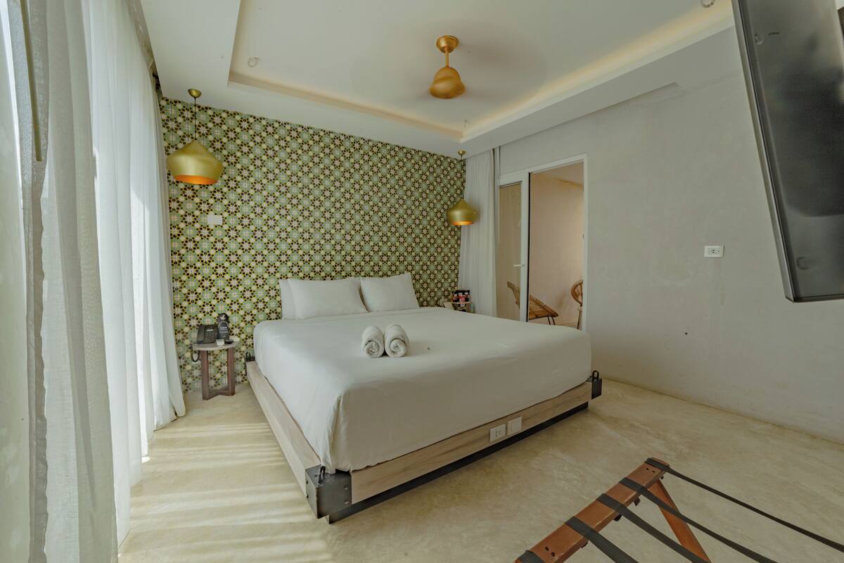 A bedroom with a bed, bedside table, lamp, and patterned wallpaper.