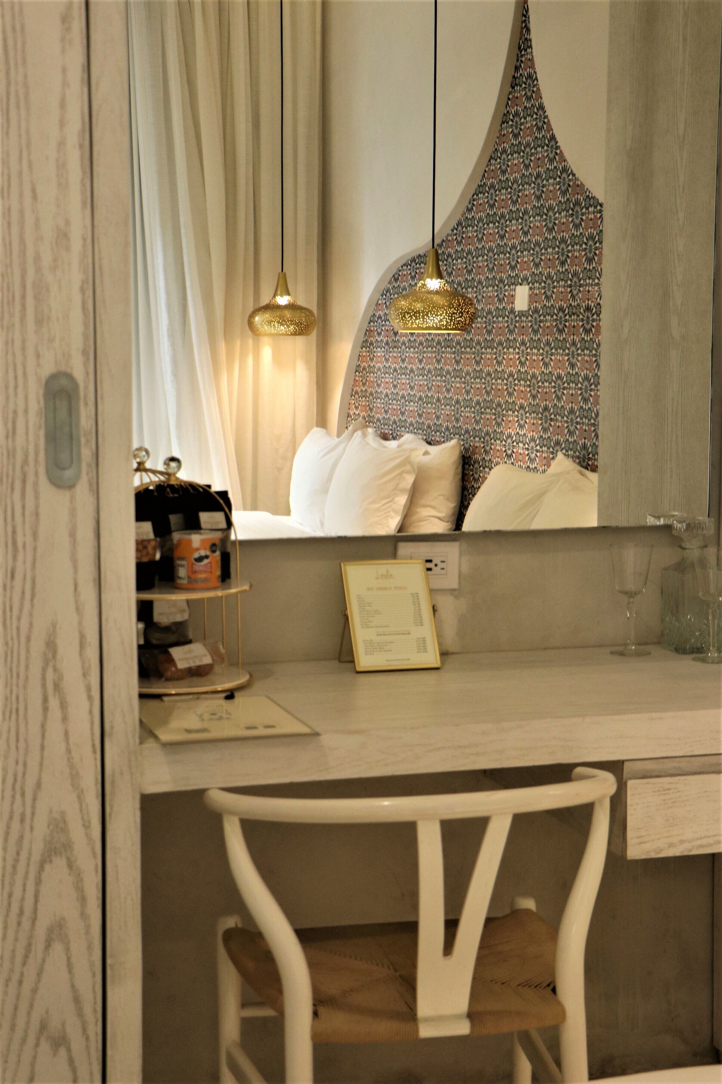 A bedroom with a wooden desk, a chair, a hanging light fixture, and a patterned wall.