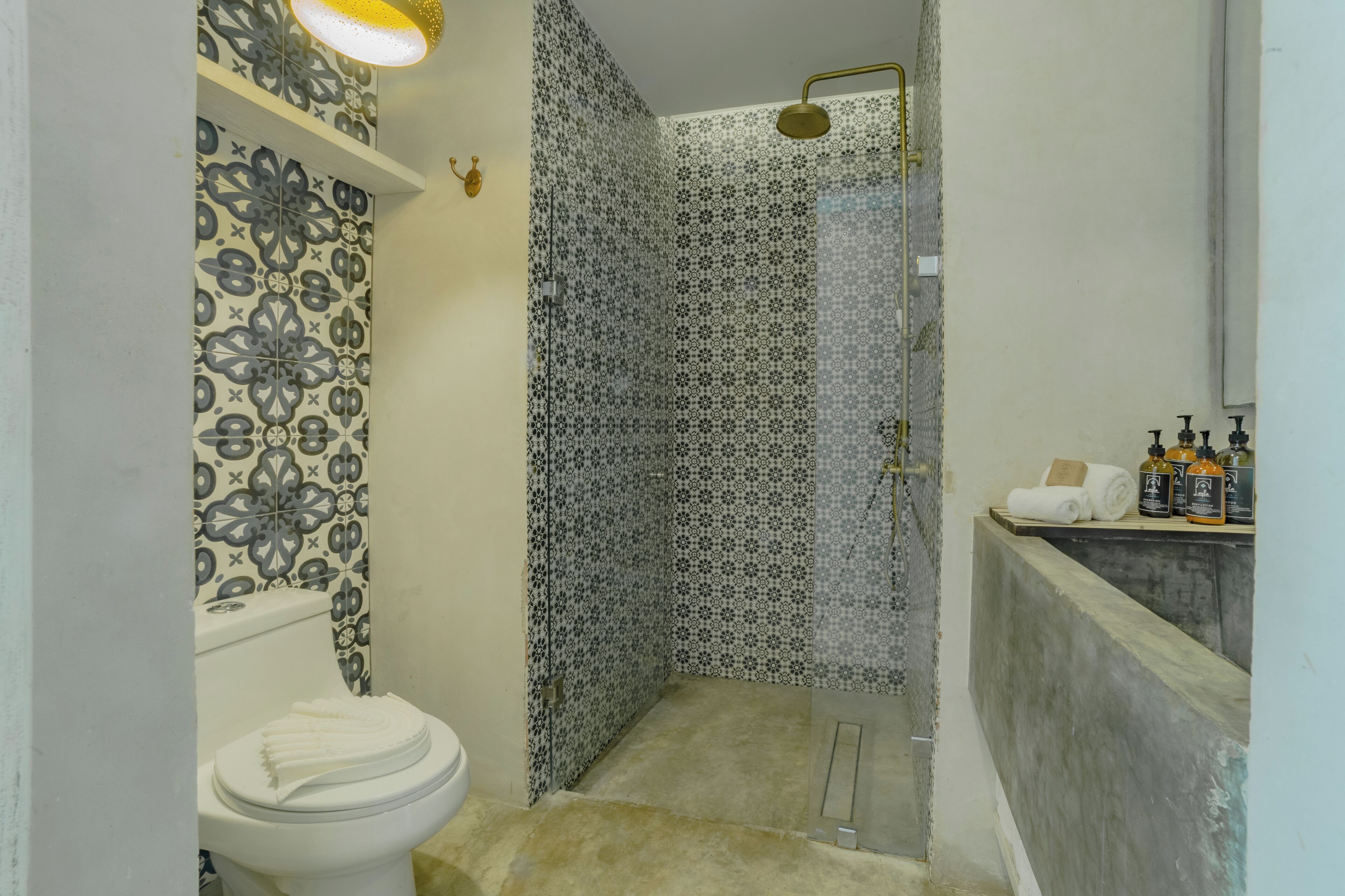 A bathroom with patterned tiles, a toilet, a shower with a glass door, and a shelf with toiletries.