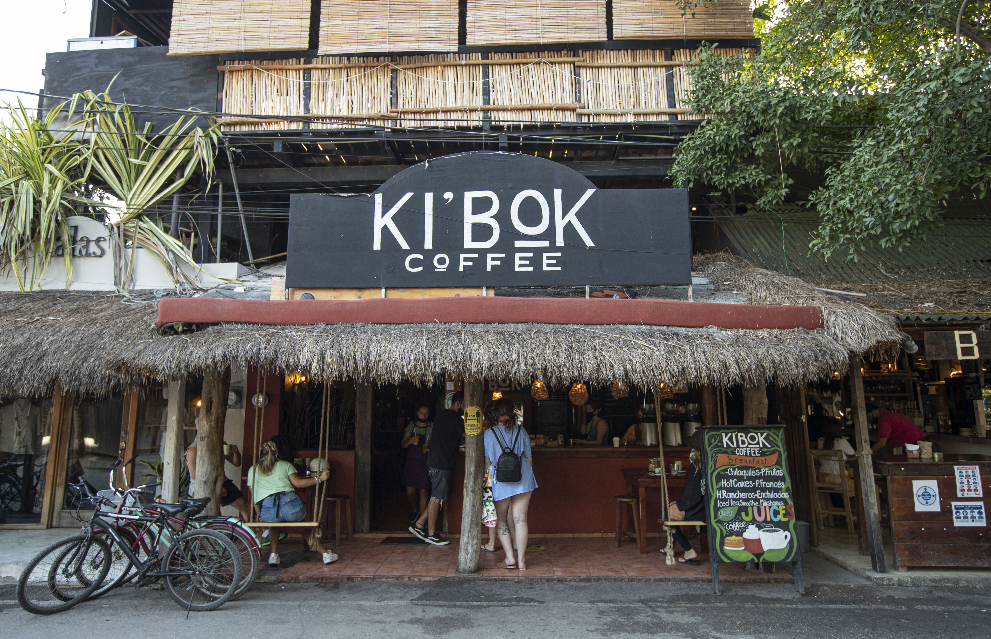 Una cafetería llamada 'Ki Bok Coffee' con techo de paja, bicicletas estacionadas afuera y un cartel que muestra los artículos del menú.
