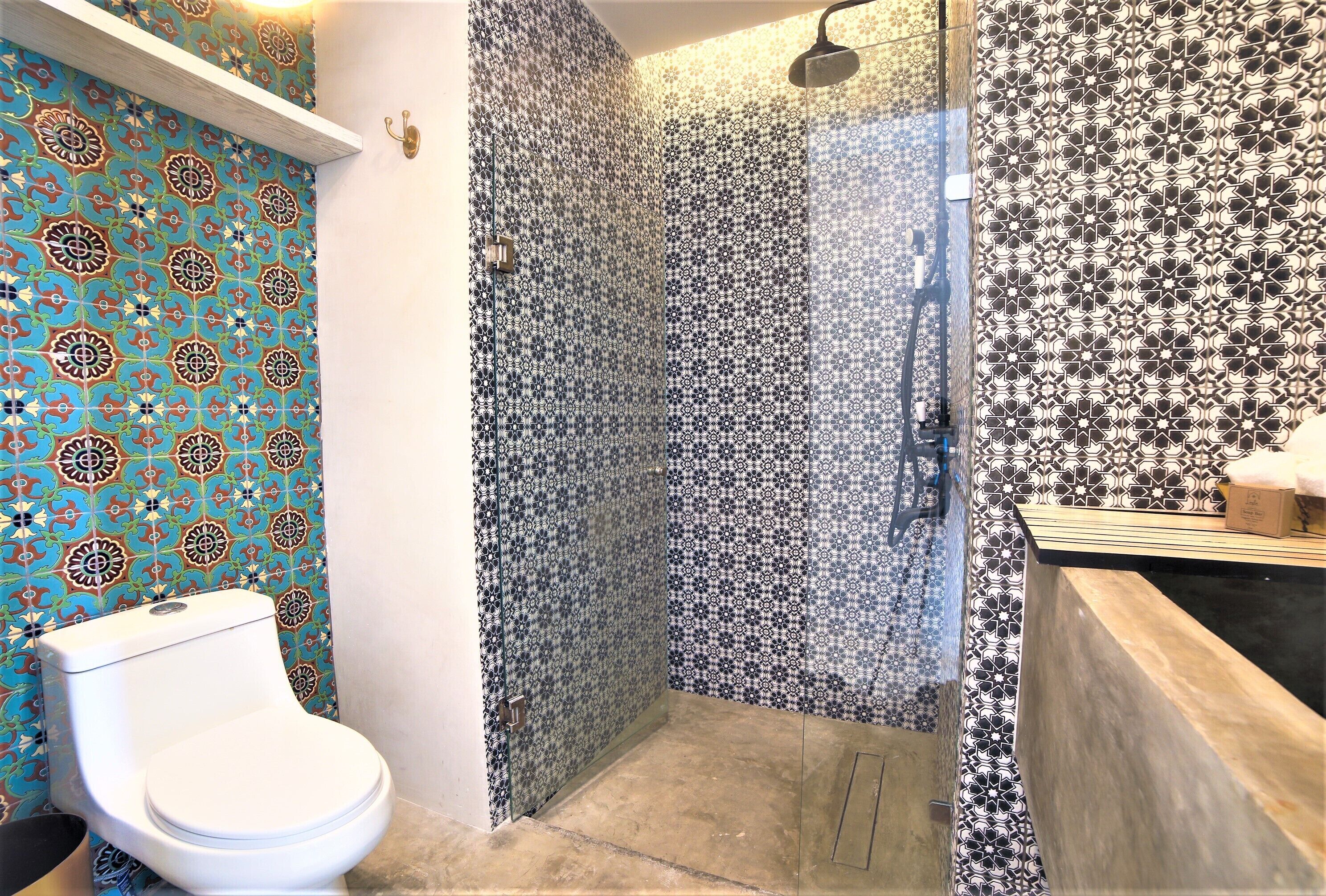 A bathroom with a toilet, a shower with patterned tiles, and a sink area.