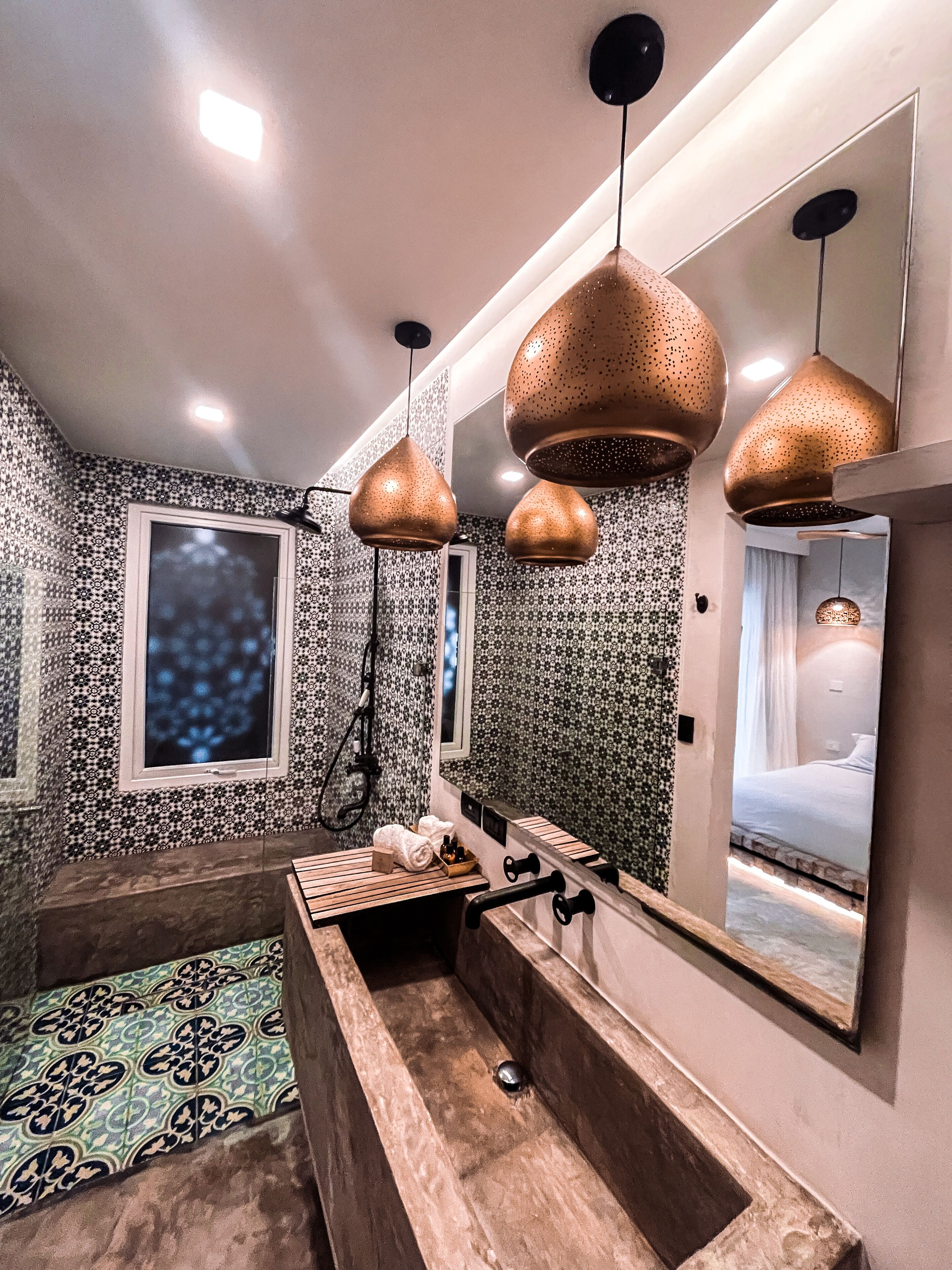 A modern bathroom with patterned walls, a large mirror, and three pendant lights.