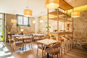 A cozy restaurant with wooden tables and chairs, stone walls, and hanging wicker lamps. - Memoria Porto FLH Hotels (Porto)
