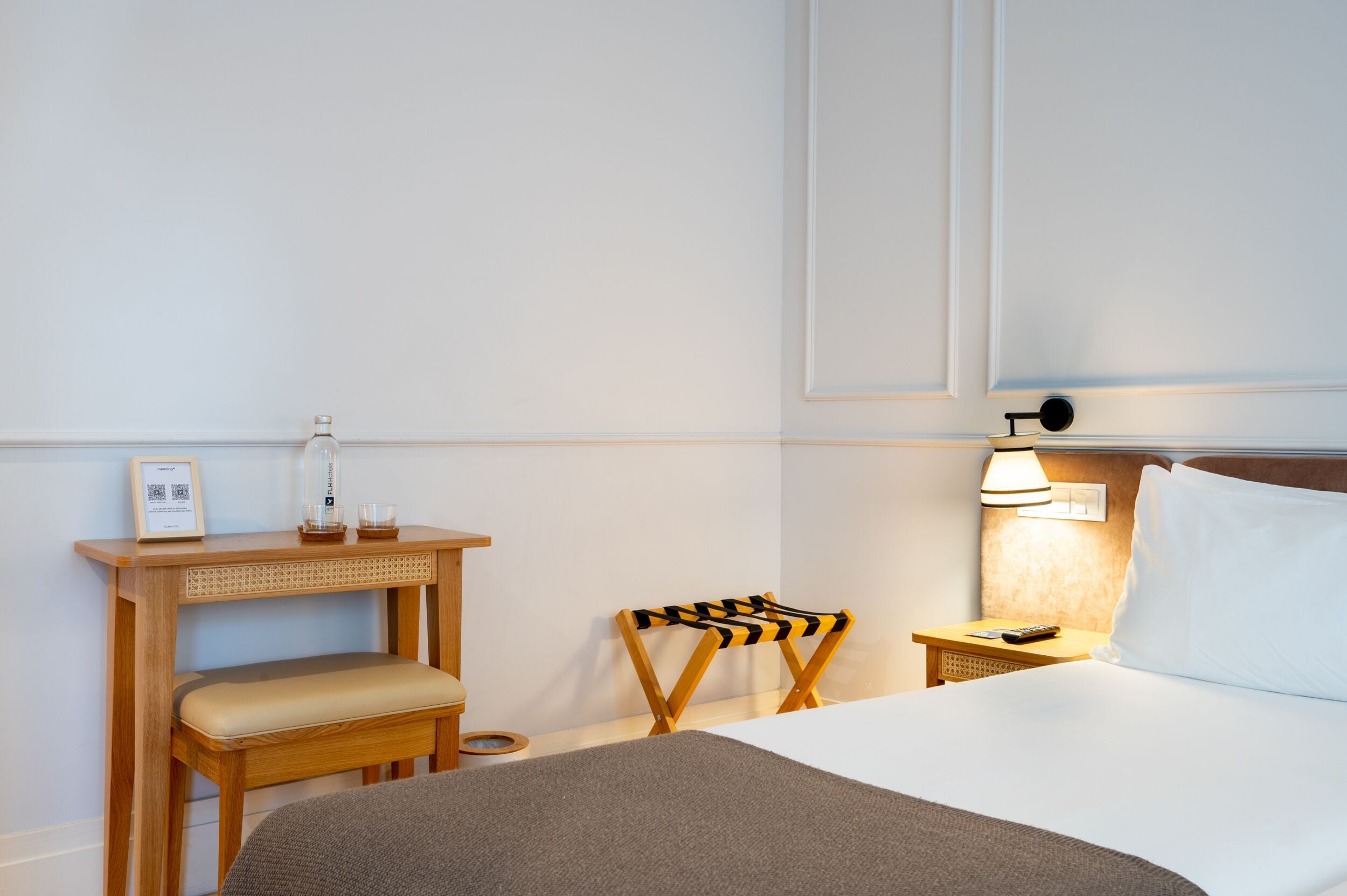 Een hotelkamer met een bed, een nachtkastje met een lamp, een kleine houten stoel en een bank.