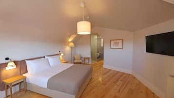 A bedroom with a bed, bedside lamps, a small table, a chair, a TV, and a wooden floor.