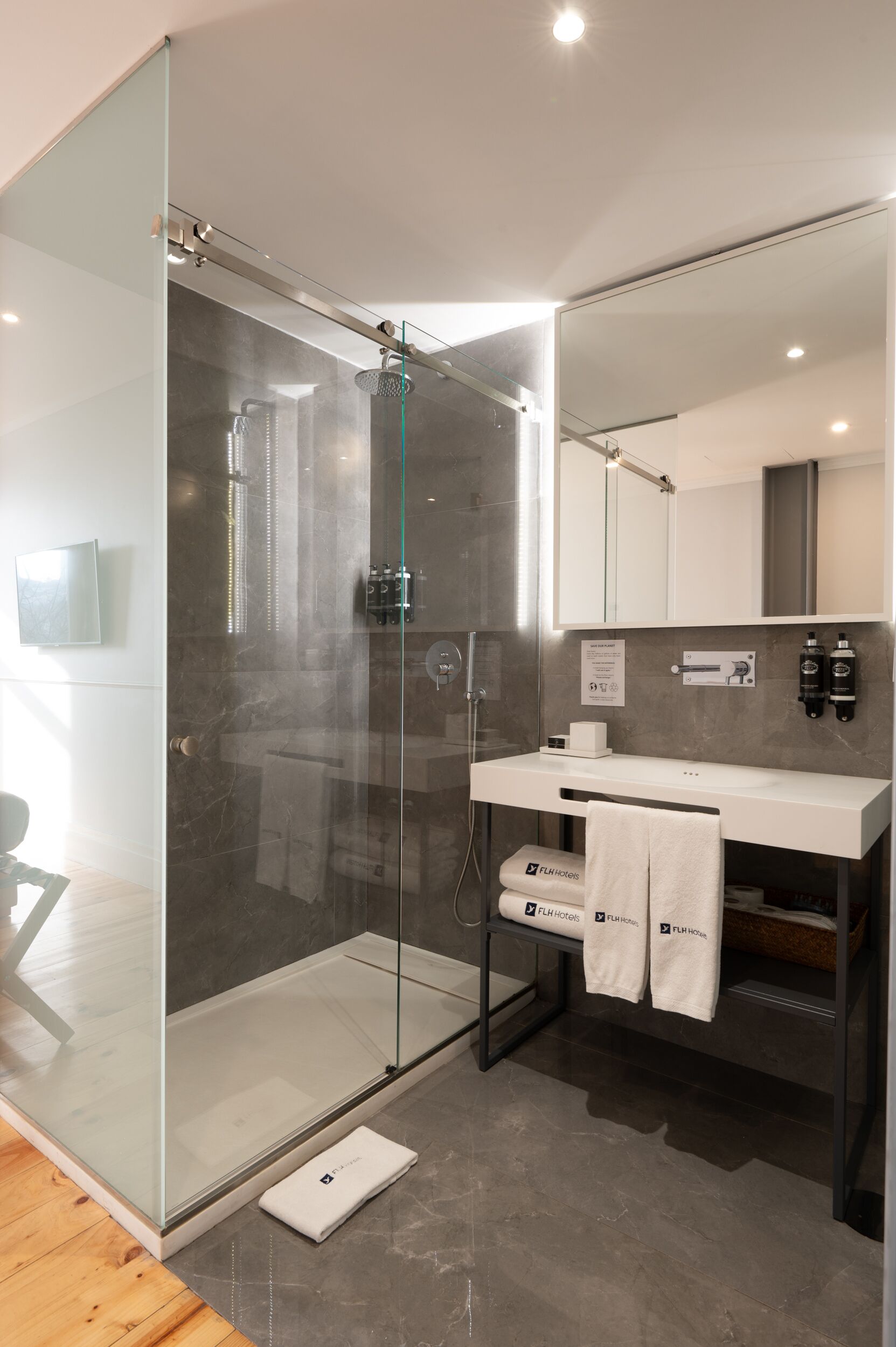 Une salle de bain moderne avec une douche à parois de verre, un meuble-lavabo blanc doté d’un porte-serviettes et un grand miroir au-dessus du lavabo.