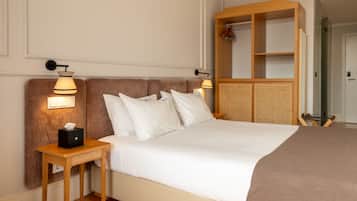 Una camera d'albergo con un letto grande, due lampade ai comodini, una testiera in legno, un tavolino con una scatola di fazzoletti e un armadio in legno con uno specchio.