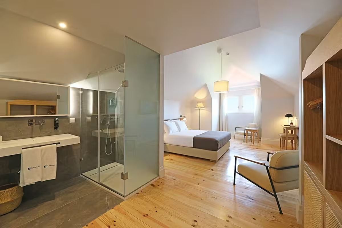 Une chambre moderne dotée d’un grand lit, d’une douche en verre, d’un plancher en bois et d’un petit coin salon avec une chaise et une table.