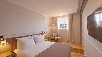 Habitación de hotel con cama, mesita de noche, lámpara, sillón y un amplio ventanal con cortinas.